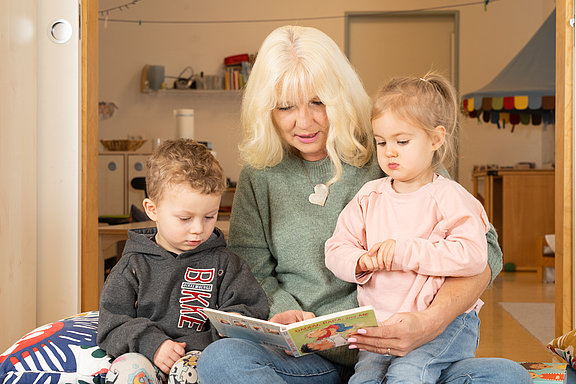 Frau schaut mit zwei kleinen Kindern ein Buch an