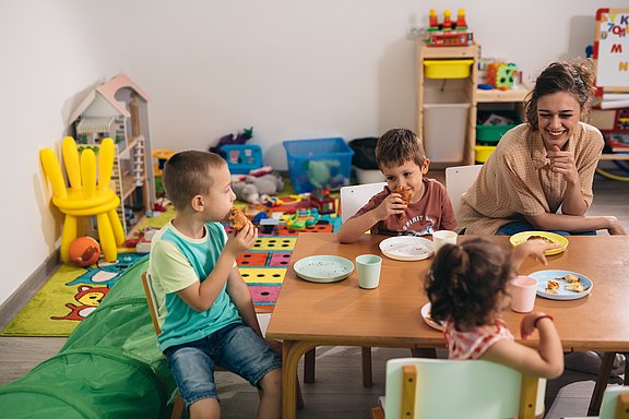 Drei Kinder sitzen am Tisch in der Kita und essen.